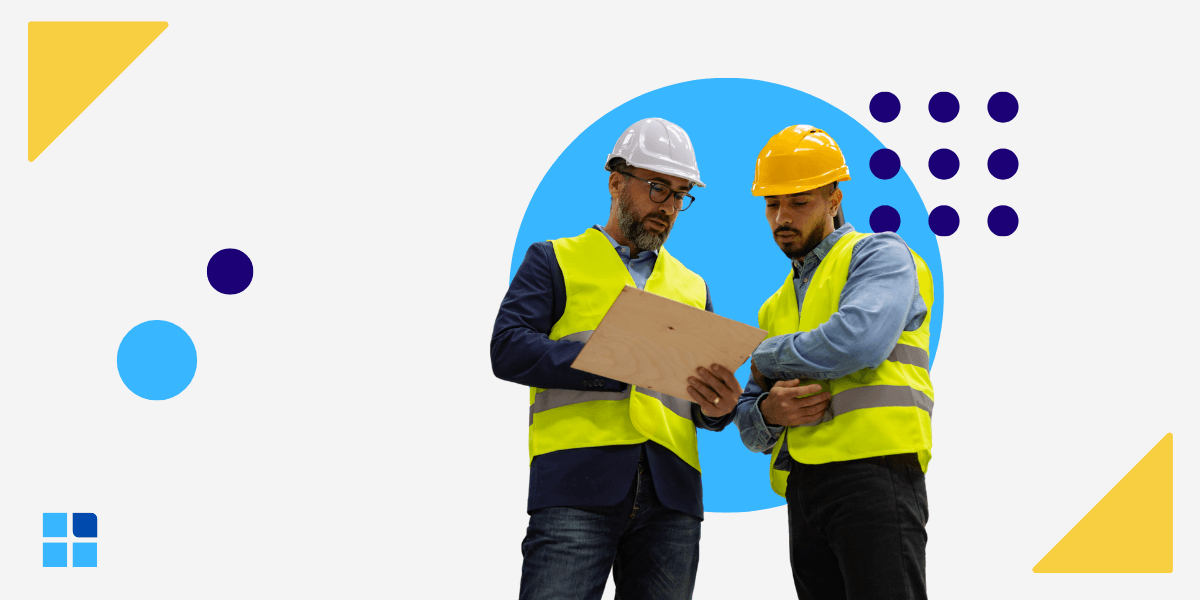 Two construction workers in safety vests and helmets study a clipboard.