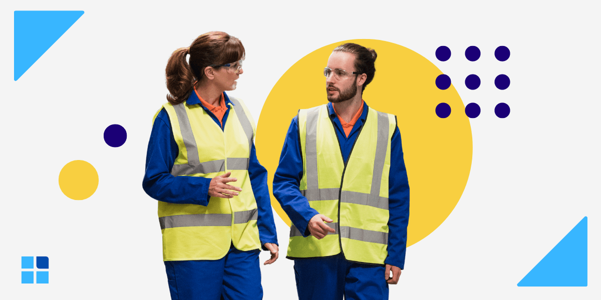 Two workers in blue uniforms and yellow safety vests converse.