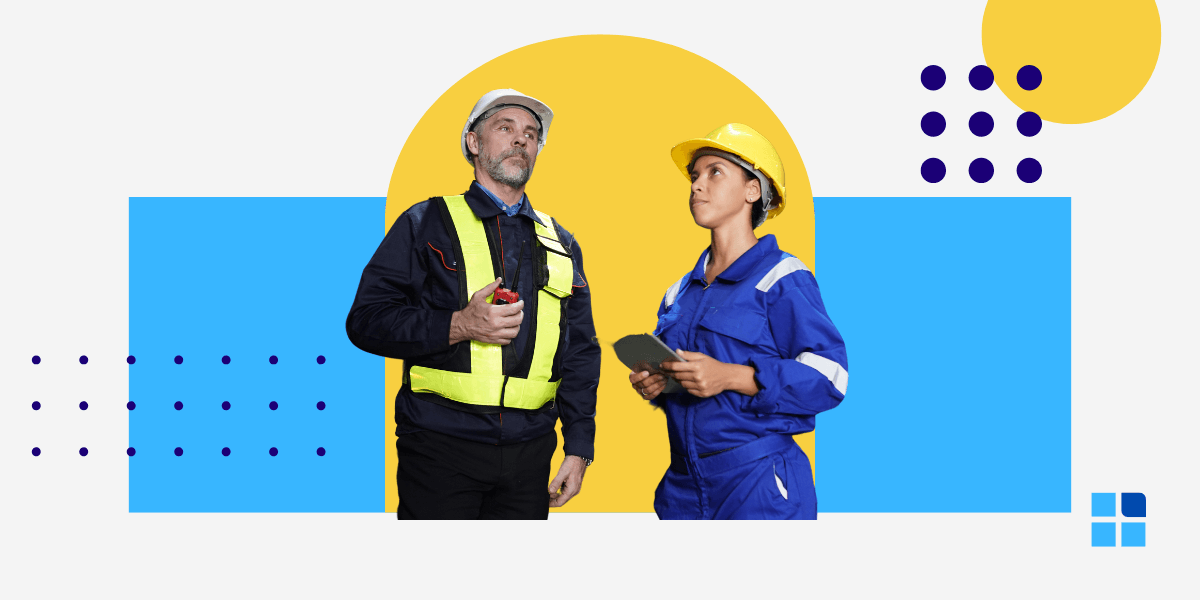 Two construction workers in safety gear, one holding a clipboard, stand together.