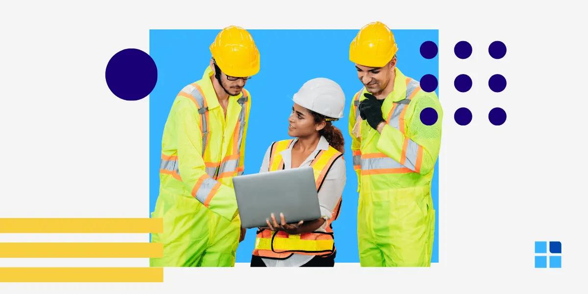 Three construction workers in safety gear and helmets discuss while looking at a laptop.