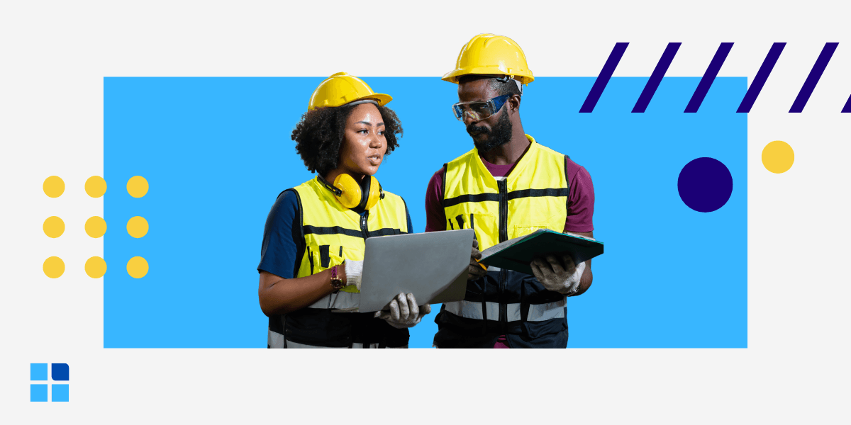 Two construction workers wearing yellow helmets and vests discuss plans on a tablet and clipboard.