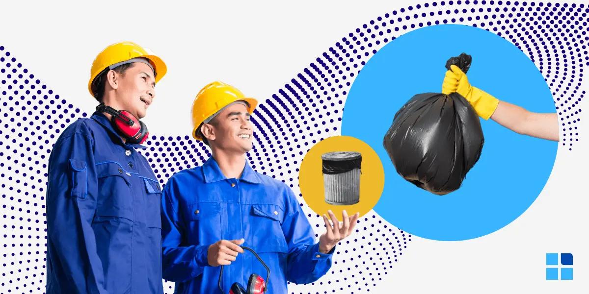 2 workers in blue uniforms & yellow helmets smile, standing beside a trash bin a& a garbage bag,