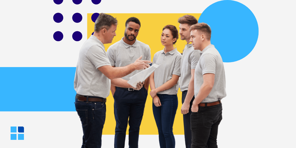 A group of five people in gray shirts stand attentively as one person discusses a document.