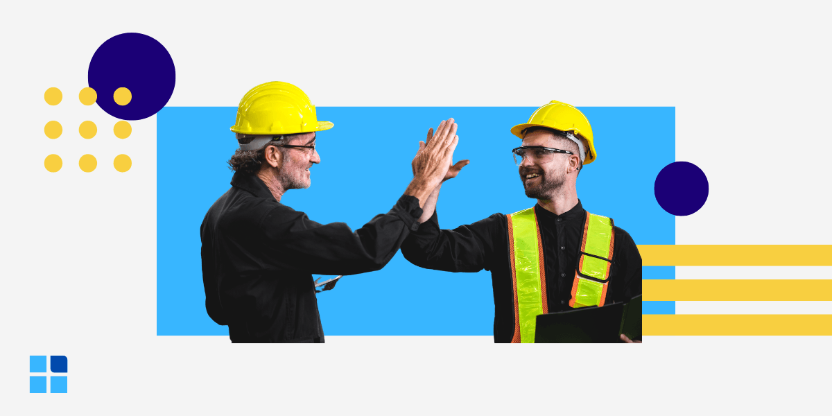 Two construction workers wearing yellow hard hats and vests high-five, smiling.