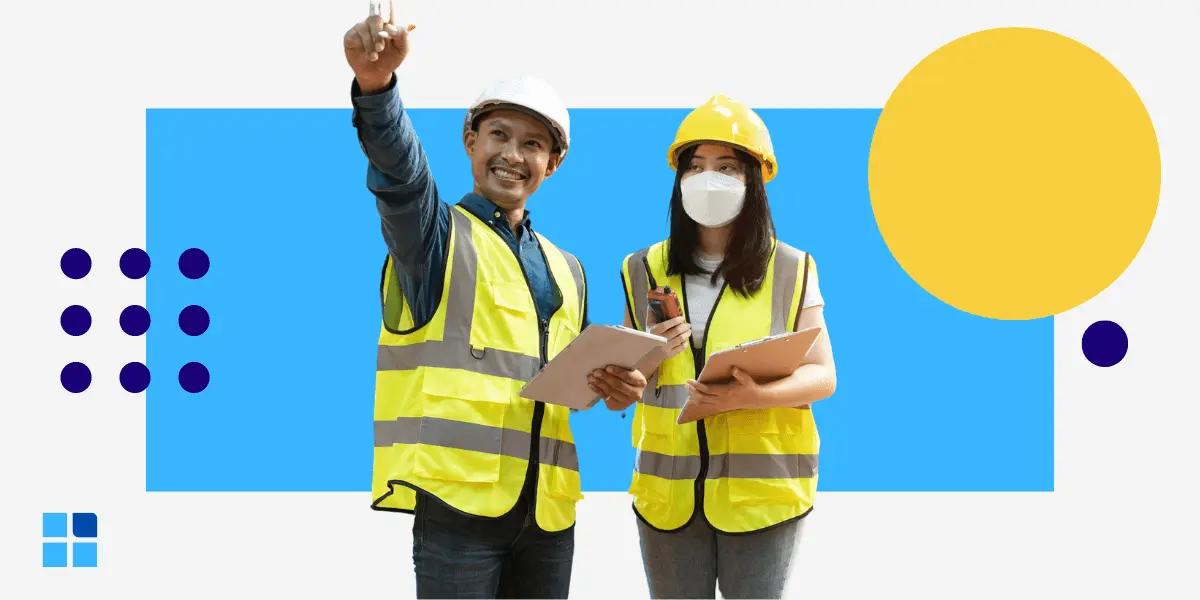 Two construction workers in safety vests and helmets stand smiling.