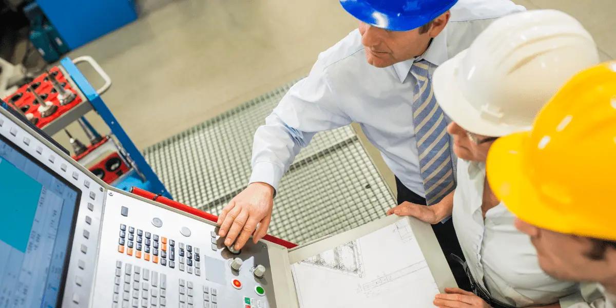 Three people wearing hard hats and formal attire are gathered around a control panel.