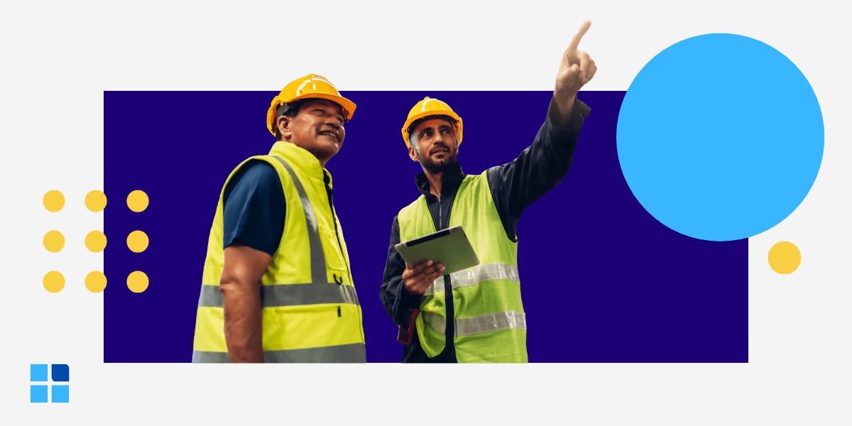 Two construction workers in yellow vests and helmets discuss plans.