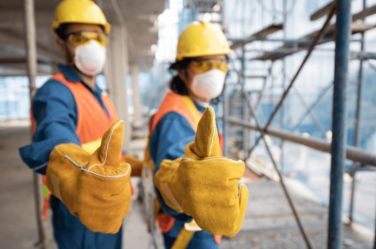 Two construction workers in full safety gear give a thumbs-up.
