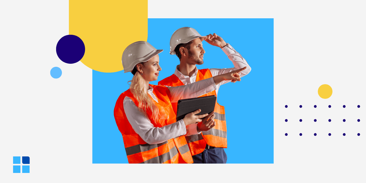 Two industrial workers in hard hats and orange vests analyze data on a tablet and point forward.
